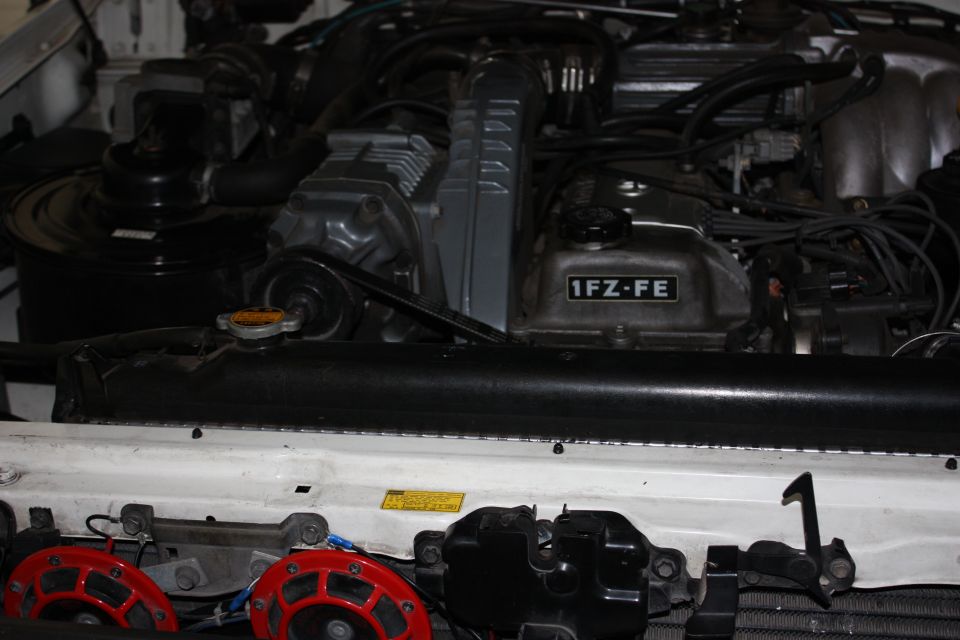 engine bay with 1FZ-FE marking on valve cover, red horns visible below radiator