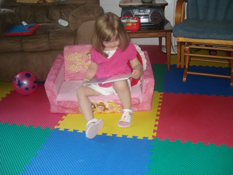 2000 Ford Crown Victoria - A young girl sits on a pink couch, engrossed in a book, surrounded by colorful floor mats.