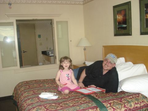 2000 Ford Crown Victoria - A man and a young girl are relaxing on a hotel bed, with a pass-through window revealing a bathroom area.