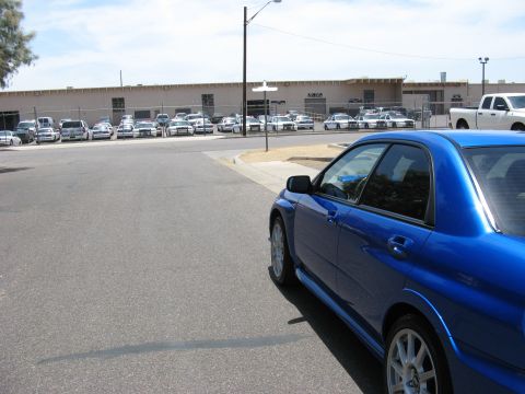 2005 Subaru Impreza - A blue Subaru WRX STI is parked on the street, with a line of police cars in the background.