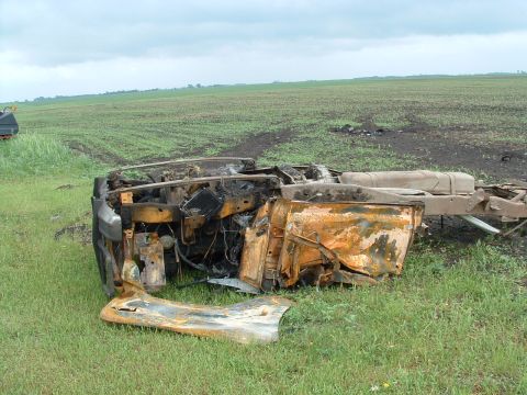 1988 Ford F-150 - This severely damaged truck chassis rests on its side in a field, showing extensive fire damage.