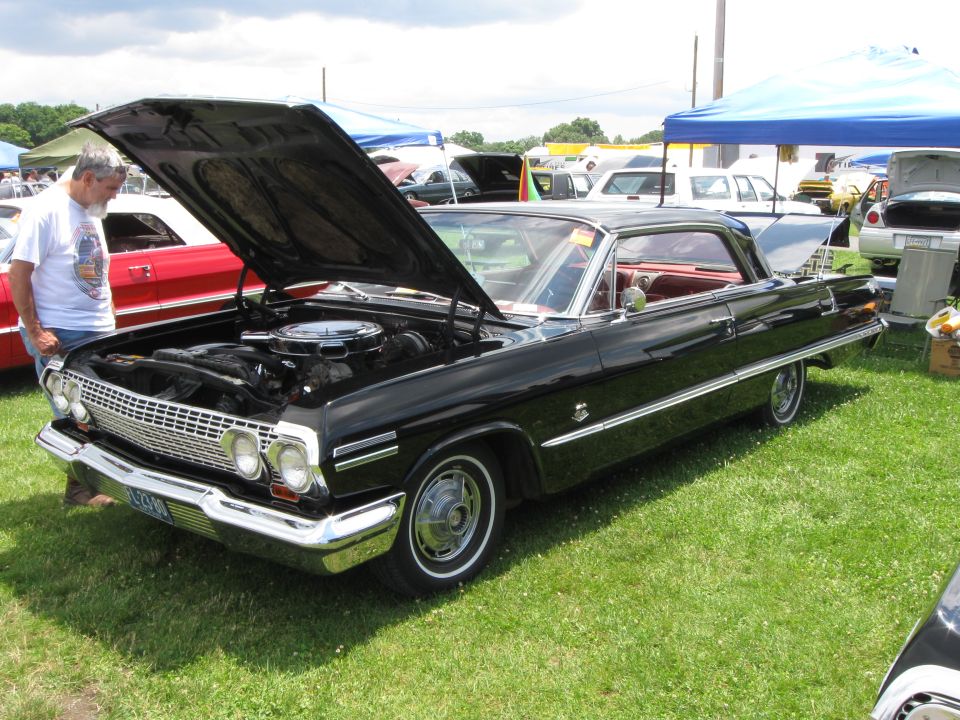 Black 1963 Chevrolet Impala convertible with hood open, red interior, chrome trim, and a license plate reading "L23496"