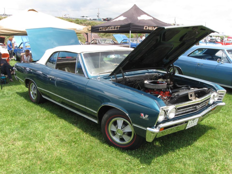 Teal 1967 Chevelle SS convertible with hood open, parked on grass next to another blue car