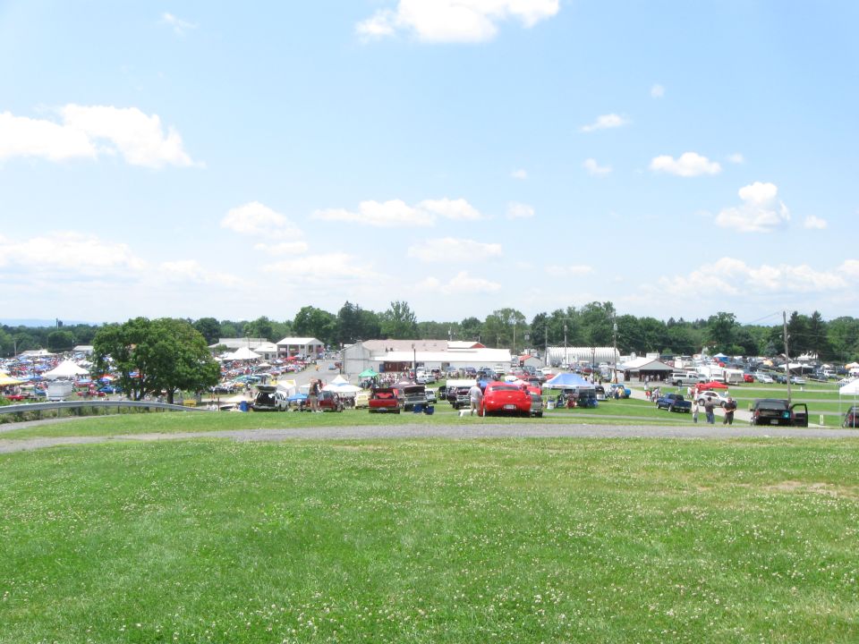 Outdoor car show with many vehicles parked and tents set up on a sunny day