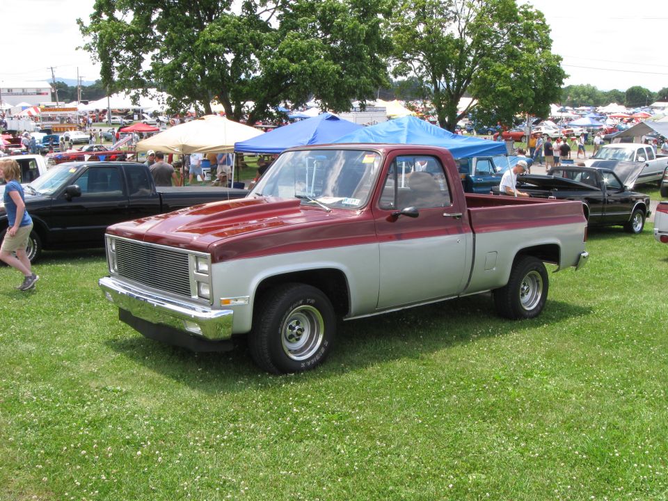 Two-tone red and silver pickup truck parked on grass at an outdoor event