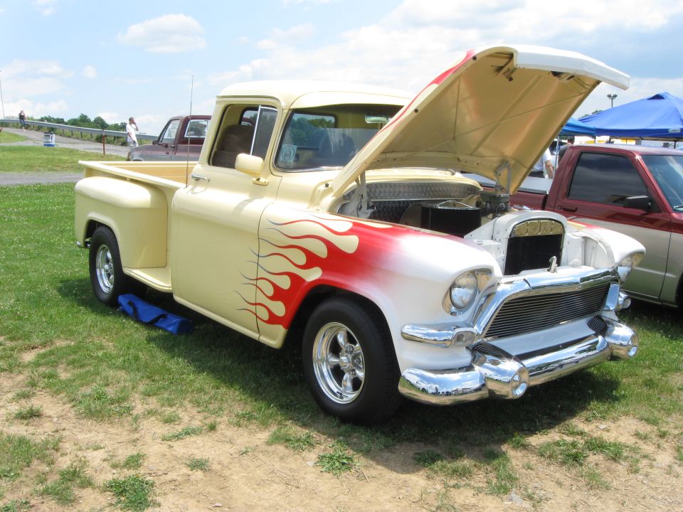 Cream and white pickup truck with red and yellow flames, hood open, chrome grille, and custom wheels