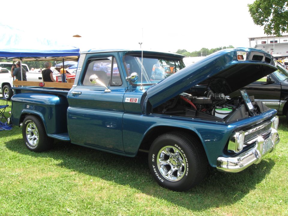 Blue pickup truck with hood open, showing engine. Chrome wheels and trim. Another truck visible behind it