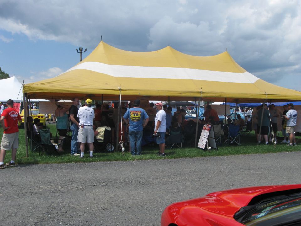 People stand under a large yellow tent with a white stripe at an outdoor gathering