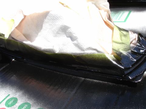 1993 Ford Taurus - A close-up view of an automotive part being masked and painted, with paper towels and tape protecting certain areas.
