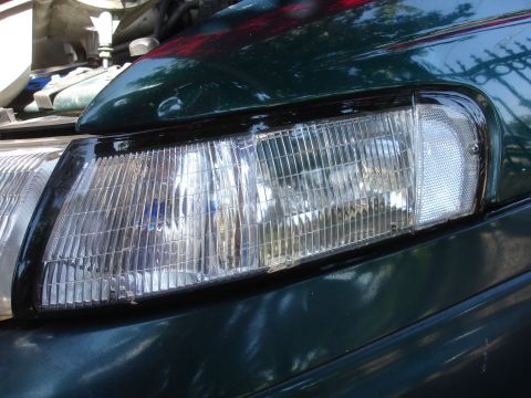 1993 Ford Taurus - Close-up of a green 1992 Ford Taurus headlight assembly, showing the ribbed main beam and clear turn signal lens.