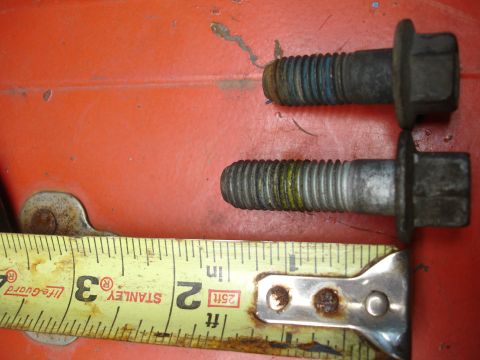 1990 Ford Taurus - Two bolts, one with blue markings and the other with yellow, are measured against a tape measure on an orange surface.