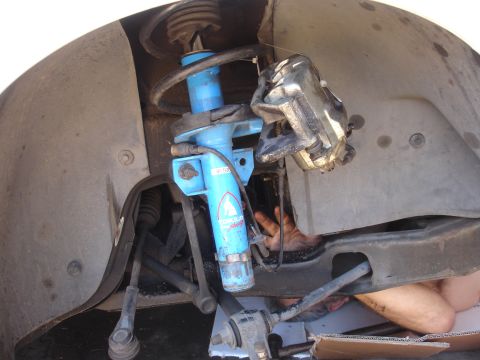 1990 Ford Taurus - Close-up view of a vehicle's front suspension and brake system, with a person's arm reaching into the assembly.