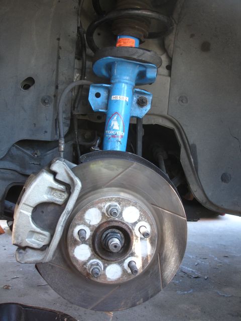 1990 Ford Taurus - Close-up of a front brake assembly a blue Tokico shock absorber and a slotted rotor, likely part of a brake upgrade.