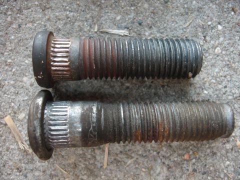 1990 Ford Taurus - Two used wheel studs are shown on a concrete surface, exhibiting signs of rust and wear.