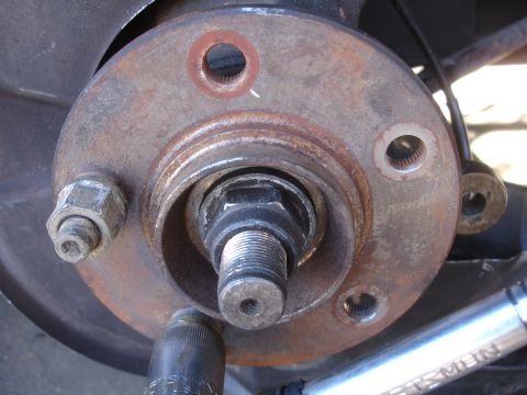 1990 Ford Taurus - Close-up view of a rusty front brake rotor and hub assembly, with a socket wrench engaged on a bolt.