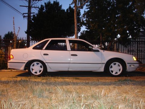1990 Ford Taurus - A white 1990 Ford Taurus sedan is parked outdoors at dusk, showing its side profile.