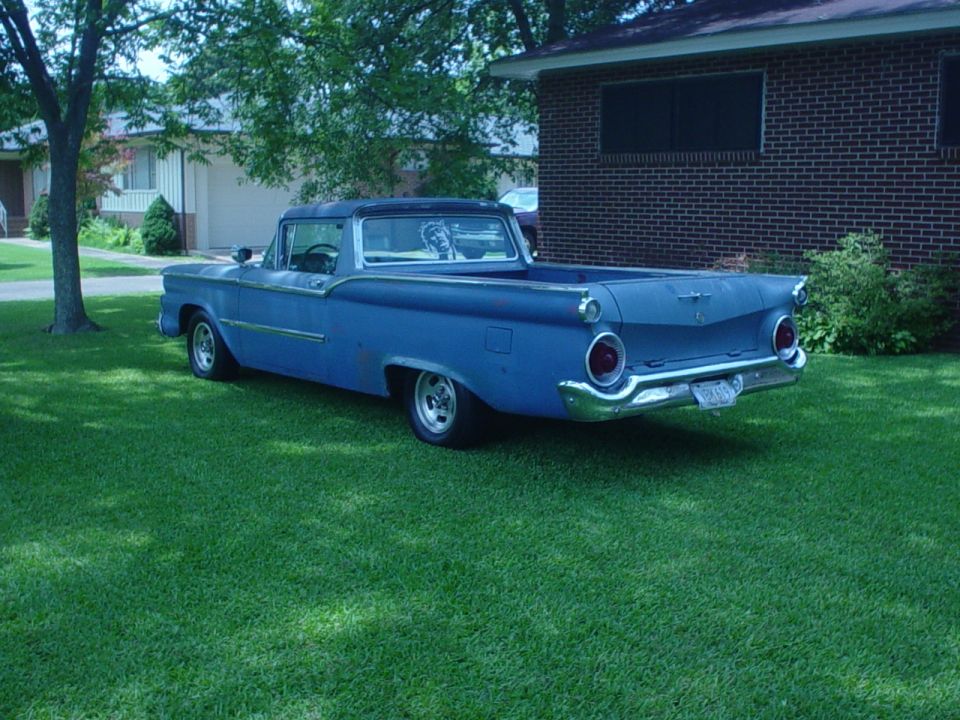 Blue late-1950s Ford Ranchero with primer spots and fins parked on a lawn