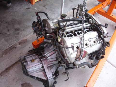 1992 Ford Taurus - A V6 engine and transmission assembly is suspended by a chain hoist, ready for installation or repair.
