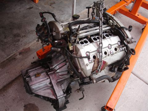 1992 Ford Taurus - An engine and transmission assembly is suspended by chains on an orange engine stand.