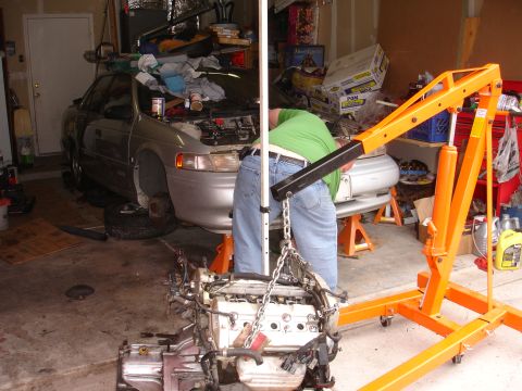1992 Ford Taurus - Engine removal in progress for a 1992 Ford Taurus, supported by jack stands in a cluttered garage.