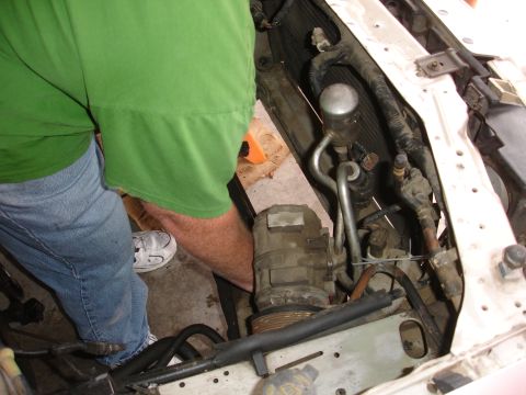 1992 Ford Taurus - Close-up view of a vehicle's engine bay, focusing on the AC compressor and associated plumbing. A person is visible working on the engine.