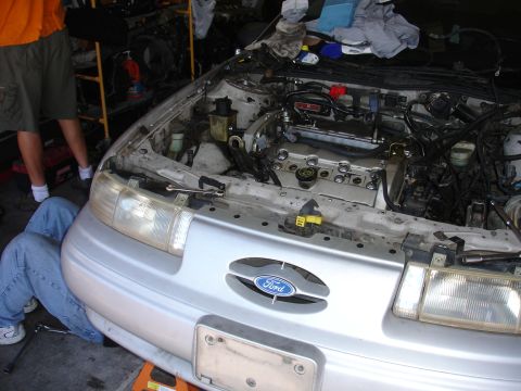 1992 Ford Taurus - Mechanic works on the engine of a silver 1992 Ford Taurus in a garage.