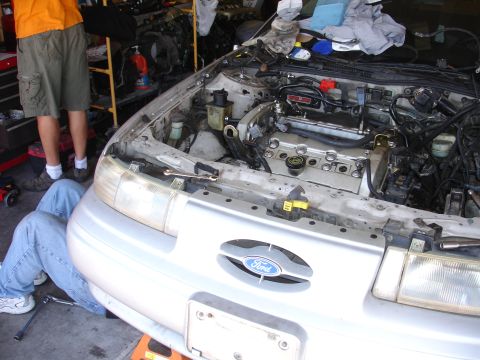 1992 Ford Taurus - Mechanics work on the exposed engine of a silver 1992 Ford Taurus during a rebuild or swap.