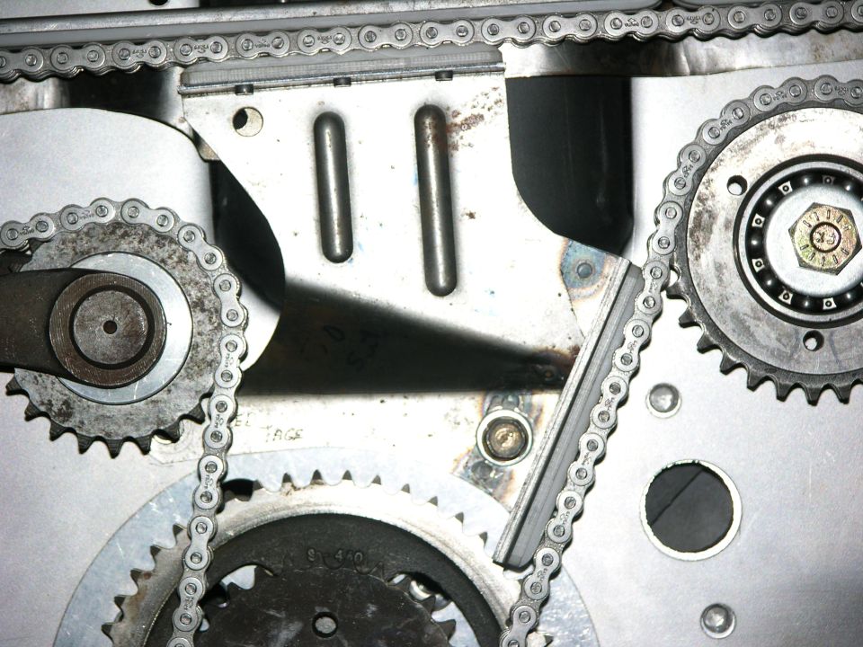 Close-up of an OHC timing chain, sprockets and plastic chain guide on a bare aluminum plate