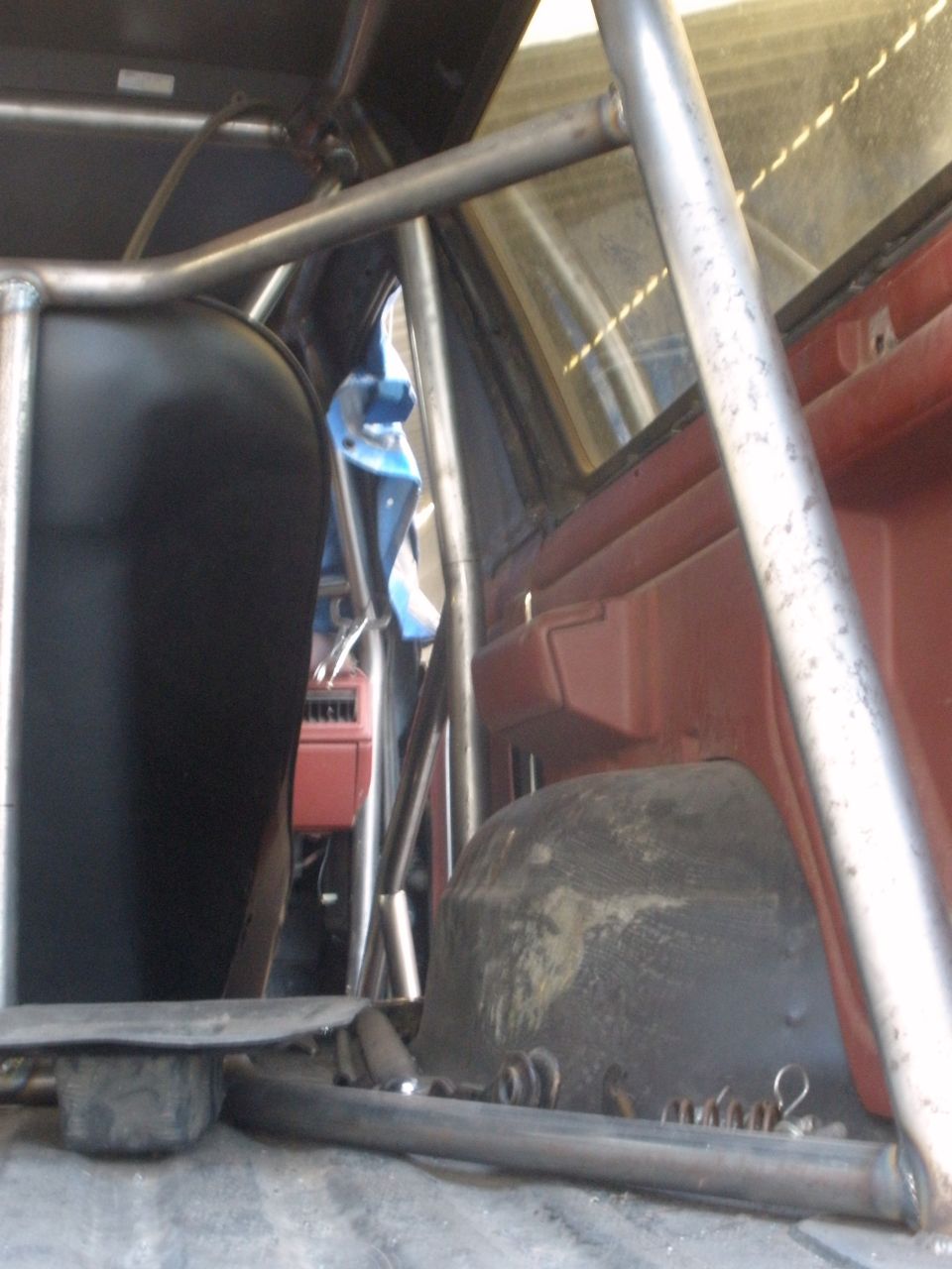 Inside a vehicle with a roll cage, fuel cell, and red interior panels visible