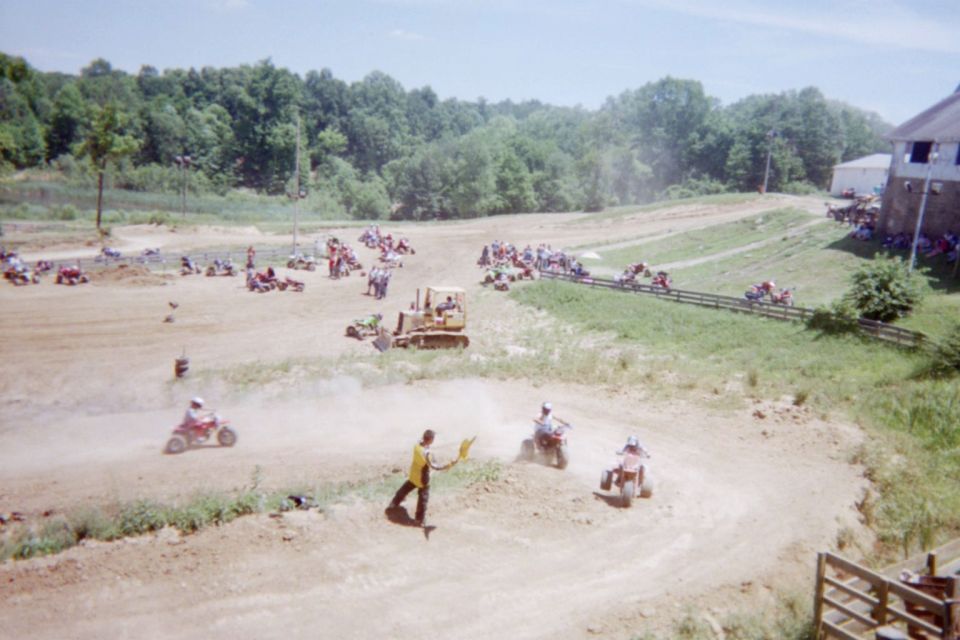 Off-road race track with ATVs, a bulldozer, and spectators. A person in yellow waves flags