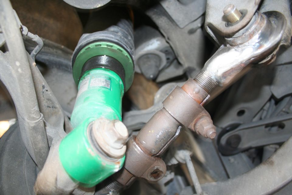 Close-up of green suspension parts and rusty metal linkage on a car's undercarriage. Text visible on green part