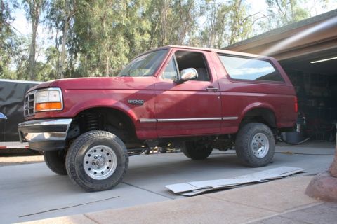 1989 Ford Bronco - This lifted red Ford Bronco SUV has a side profile view, showing its chrome trim and aftermarket wheels.