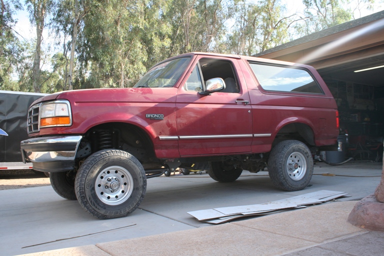 Red Ford Bronco SUV, lifted, with chrome trim and aftermarket wheels, parked outside a garage