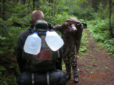 1974 Ford Ranchero - Two individuals are seen hiking on a wooded trail, with one person carrying a substantial item on their back.