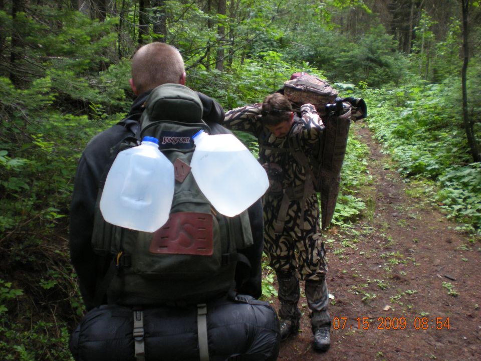 Two hikers in a forest, one carrying a large object