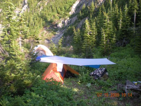 1974 Ford Ranchero - A campsite is set up in a wooded area next to a lake, with tents and a tarp providing shelter.