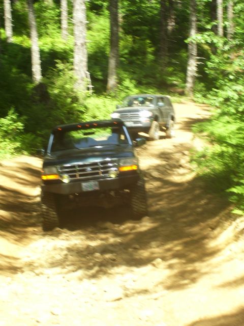 1991 Ford Bronco - Two SUVs navigate a dirt path through a wooded area.