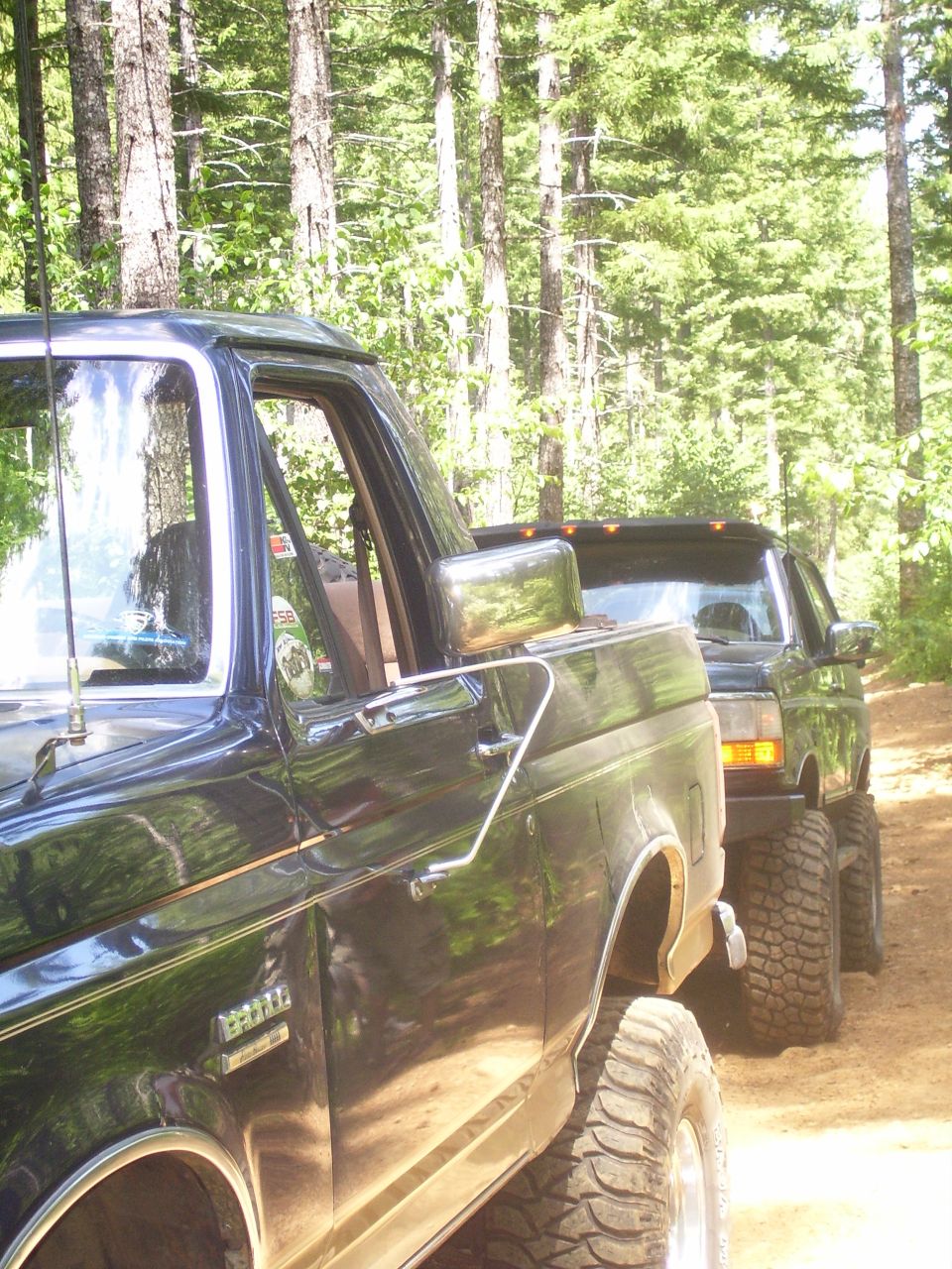 Side view of a 1991 Ford Bronco and another SUV in a forest