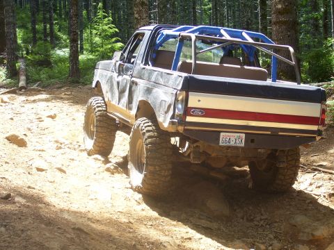 1991 Ford Bronco - Modified 1991 Ford Bronco tackling an off-road trail in a wooded area.