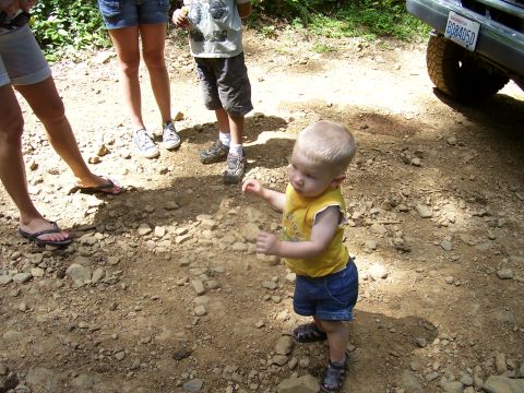 1991 Ford Bronco - A toddler stands on a rocky path while adults and another child are in the background, with a vehicle partially visible.