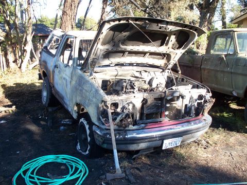 1977 Ford F-150 - This severely damaged truck sits in a yard next to another vehicle, its hood propped open.