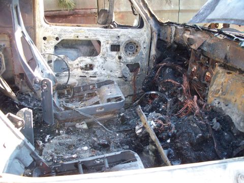 1977 Ford F-150 - The interior of a vehicle is heavily damaged by fire, with melted components and exposed wiring visible.