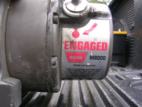 1990 Ford Bronco - Close-up of a Warn M8000 winch, showing its operational label and mounting in a truck bed.
