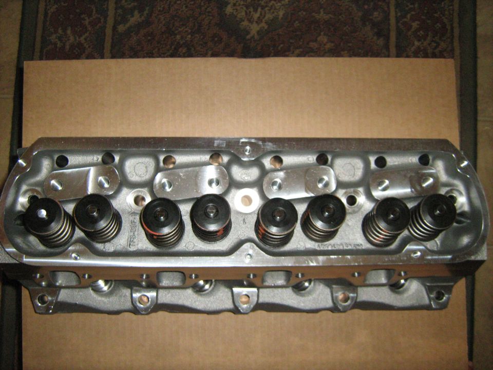Engine cylinder head with valves and springs visible. Part number visible on the side