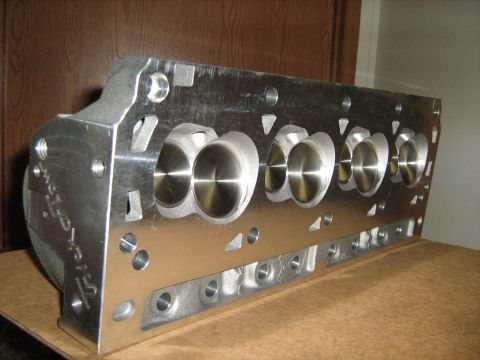 1988 Mercury Grand Marquis - A polished aluminum engine cylinder head is shown from a side angle, resting on a cardboard surface.