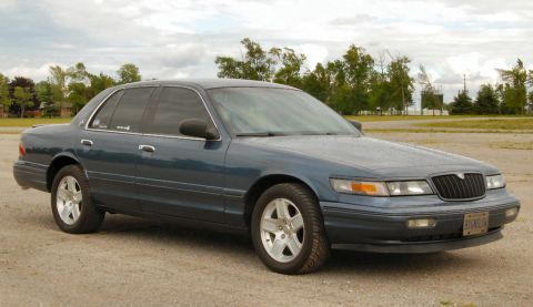 1985 Mercury Grand Marquis - A dark blue sedan, likely a Mercury Grand Marquis, is seen from the front quarter angle on a cloudy day.