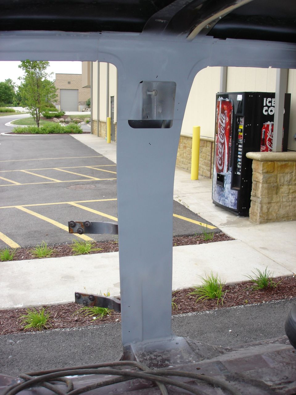 Gray painted interior pillar of a vehicle, looking out at a parking lot with vending machines