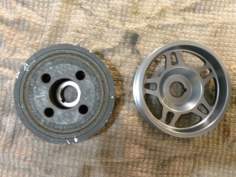 1998 Subaru Legacy - A comparison of two automotive pulleys, one appearing to be a stock harmonic balancer and the other a lighter aftermarket aluminum pulley.