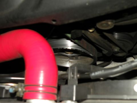 1998 Subaru Legacy - Close-up view of an engine's belt and pulley system, with a prominent red hose in the foreground.