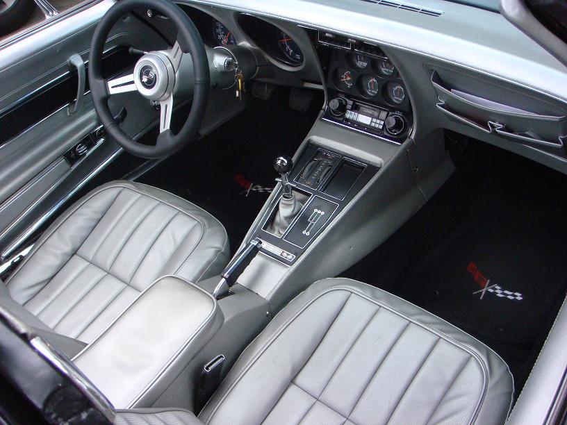 Interior of a 1975 Chevrolet Corvette showing silver leather seats, dashboard with gauges, steering wheel, and center console with automatic shifter